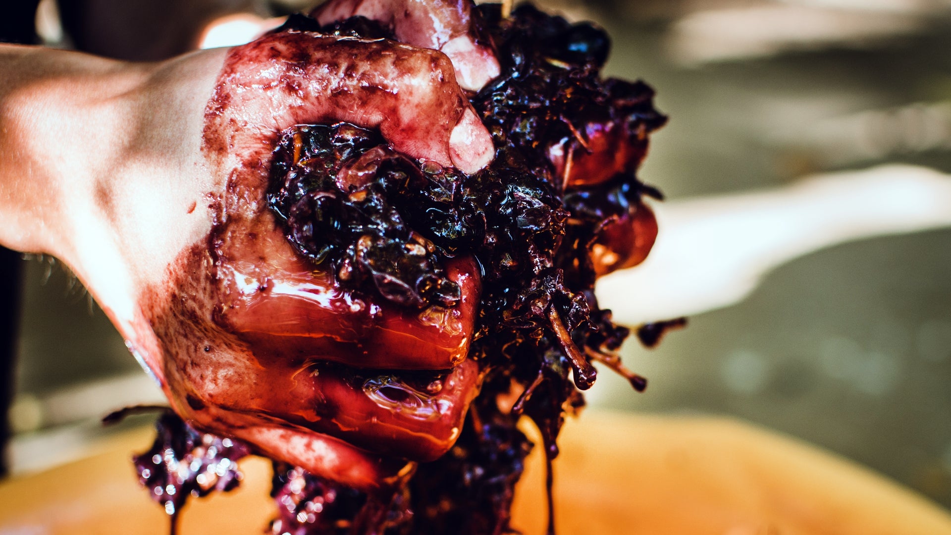Close-up of a hand squeezing dark grapes with a blurred background