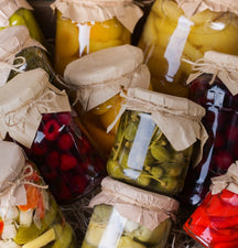Assorted jars of pickled vegetables and fruits with cloth covers.