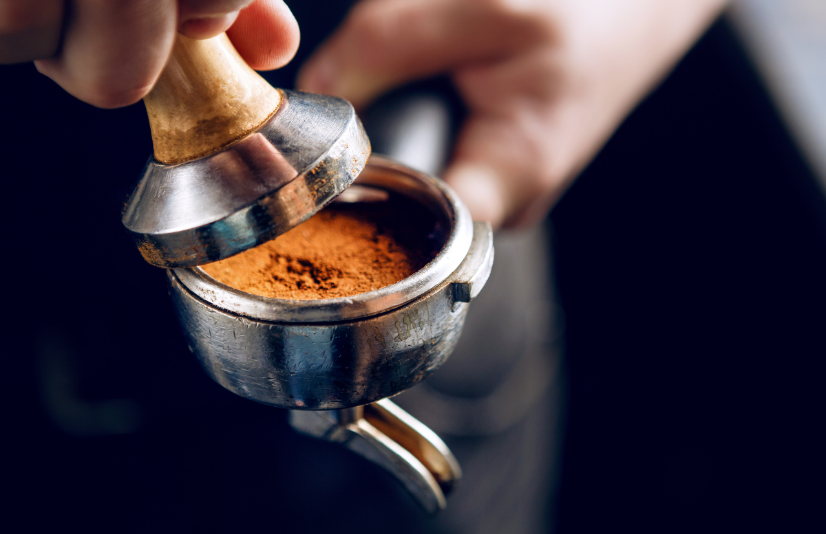Person using a coffee tamper to compress coffee grounds in a portafilter.